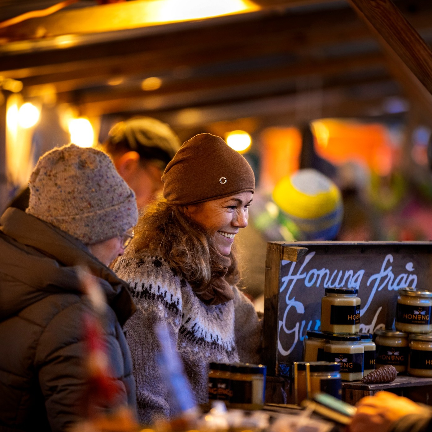 Leende kvinna står vid utställarbod på julmarknad