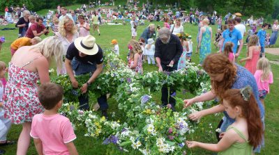 Människor reser midsommarstång på grön äng