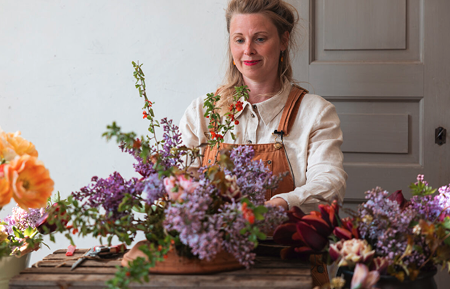 En florist binder frodiga buketter i lila och röda kulörer.