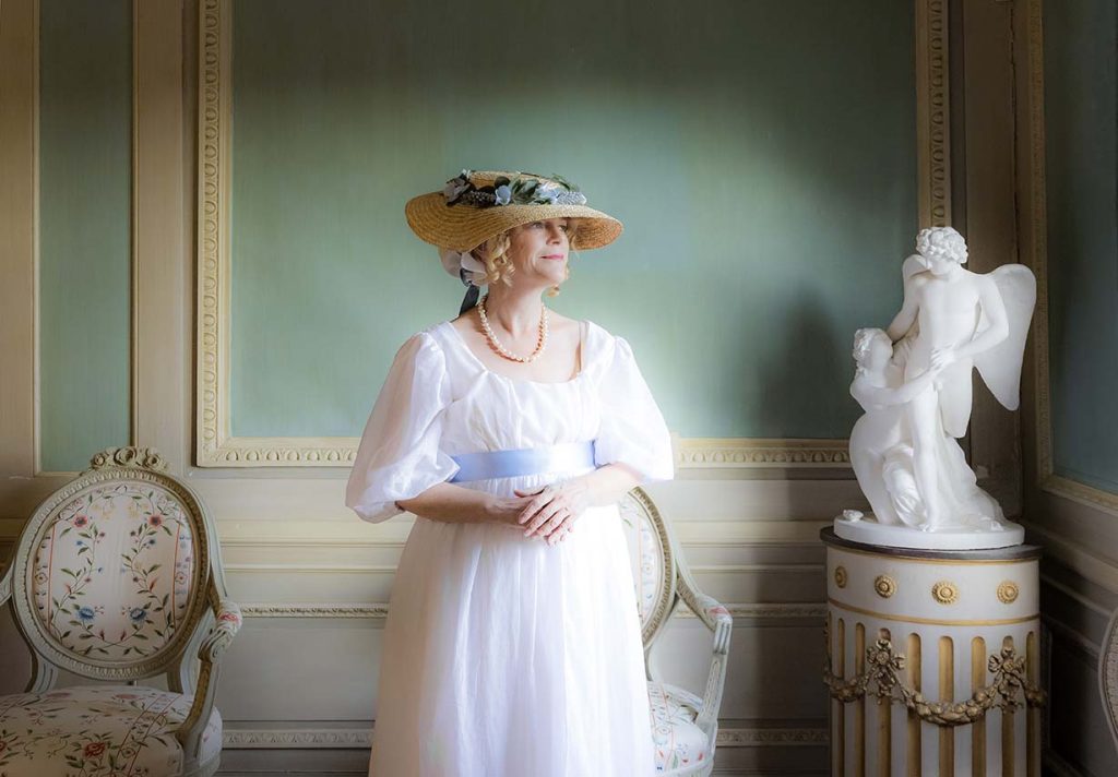 Tidsenligt klädd dam ser ut genom fönstret på Gunnebo slott.